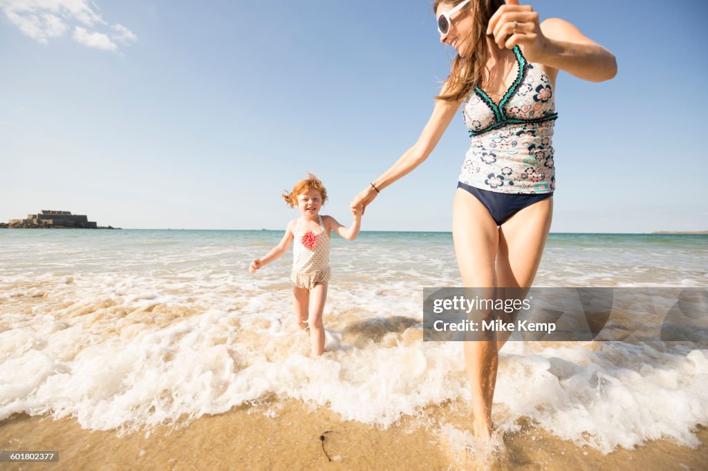 Caucasian mother and daughter playing in waves on beach