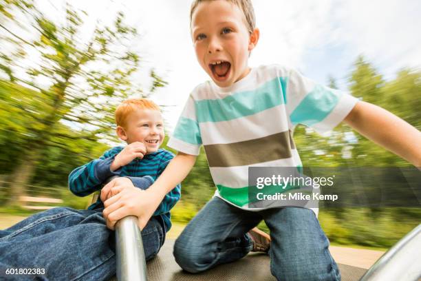 caucasian boys playing on merry-go-round - public park playground stock pictures, royalty-free photos & images