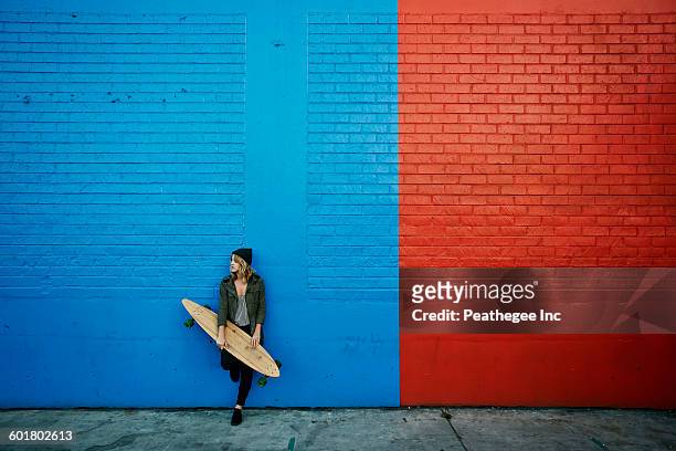 caucasian woman holding skateboard at painted wall - longboard skating stock pictures, royalty-free photos & images