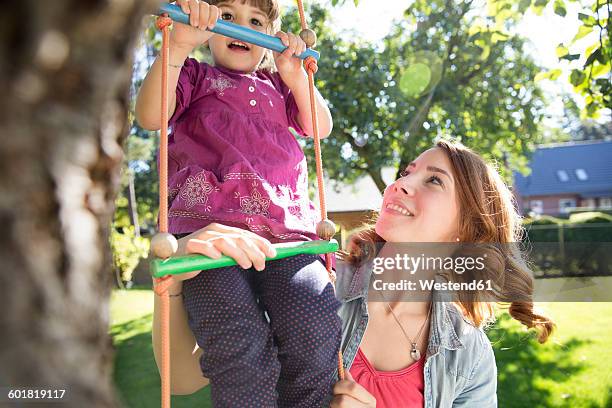 mother watching daughter on rope ladder in garden - scala di corda foto e immagini stock