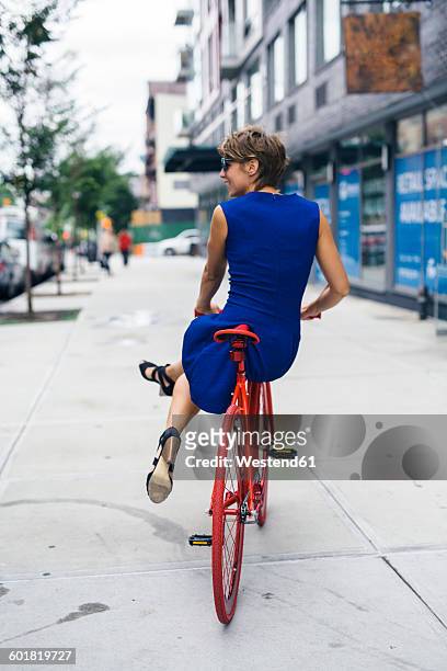usa, new york city, williamsburg, back view of smiling blond woman balancing on red bicycle - piernas en el aire fotografías e imágenes de stock