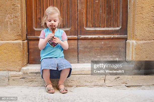 girl with chocolate ice cream cone sitting on stoop - girl eating messy ice cream cone stock-fotos und bilder
