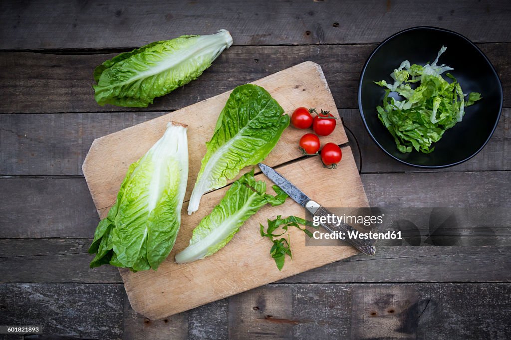 Chopped and whole romaine lettuce, pocket knife and tomatoes on wooden board