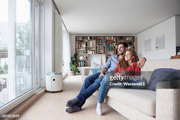 relaxed couple at home on couch looking out of window - couple couch imagens e fotografias de stock