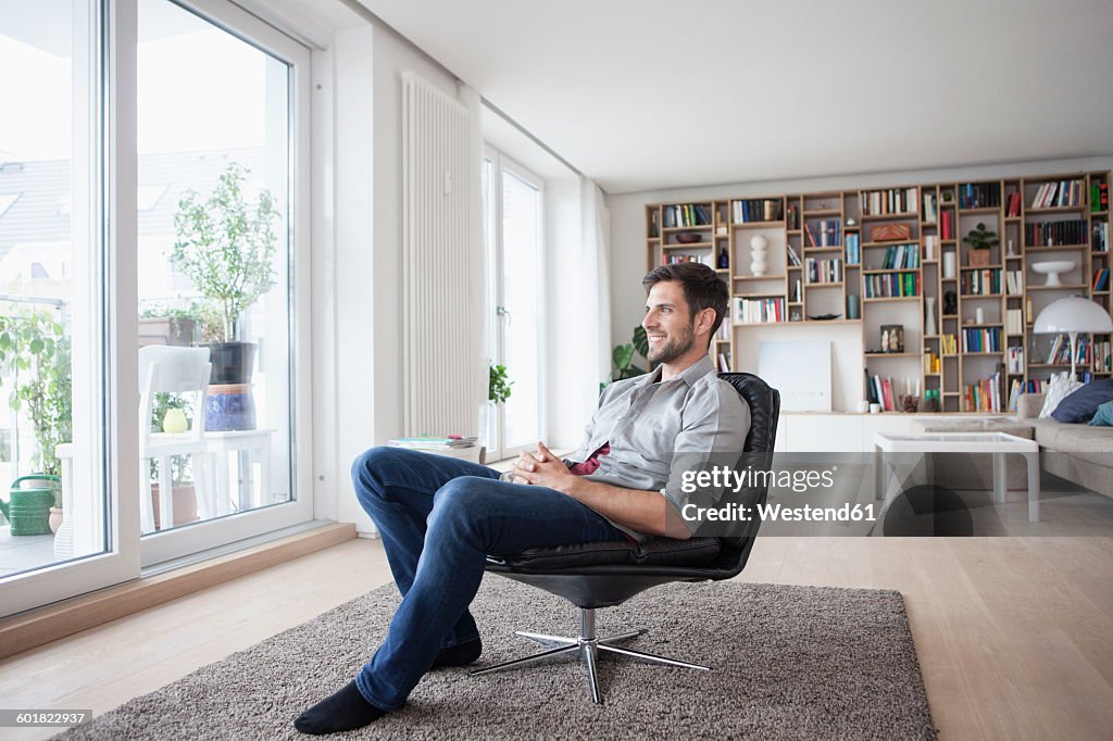 Smiling man at home sitting in armchair looking out of window