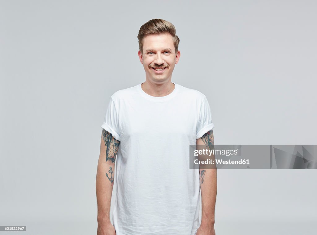 Portrait of smiling man with tatoos on his arms wearing white t- shirt in front of grey background