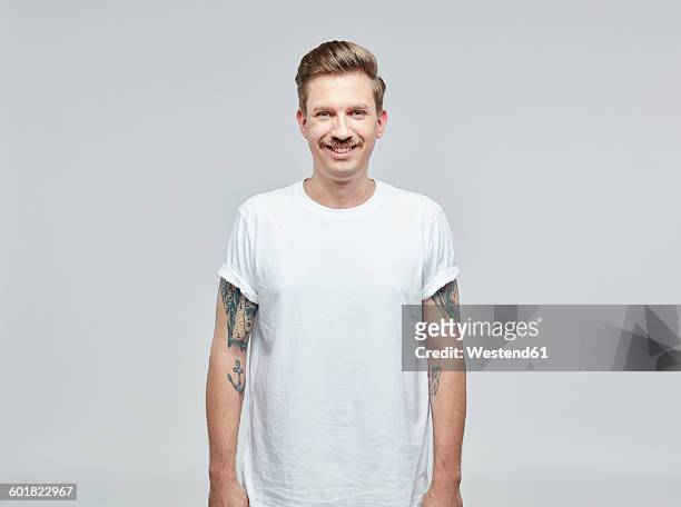 portrait of smiling man with tatoos on his arms wearing white t- shirt in front of grey background - white people stock pictures, royalty-free photos & images