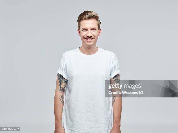 portrait of smiling man with tatoos on his arms wearing white t- shirt in front of grey background - 白人 個照片及圖片檔