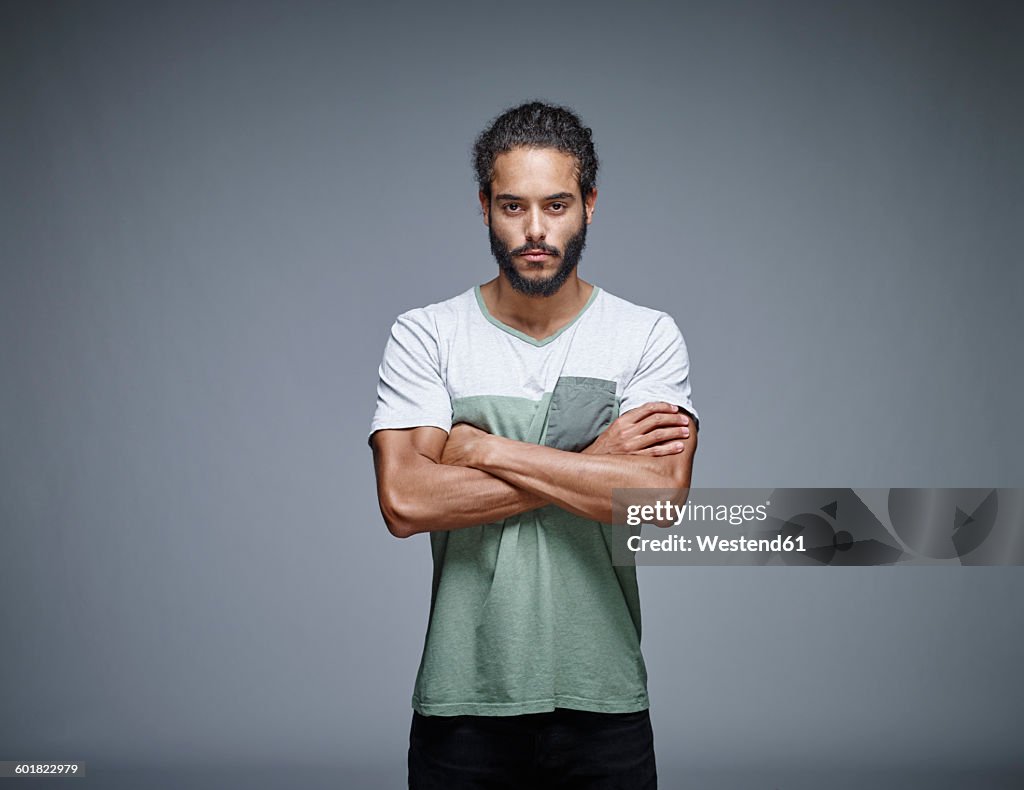 Portrait of bearded young man with crossed arms in front of grey background