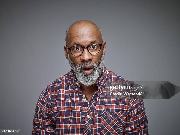 portrait of astonished man wearing spectacles and checked shirt in front of grey background - bee photos et images de collection