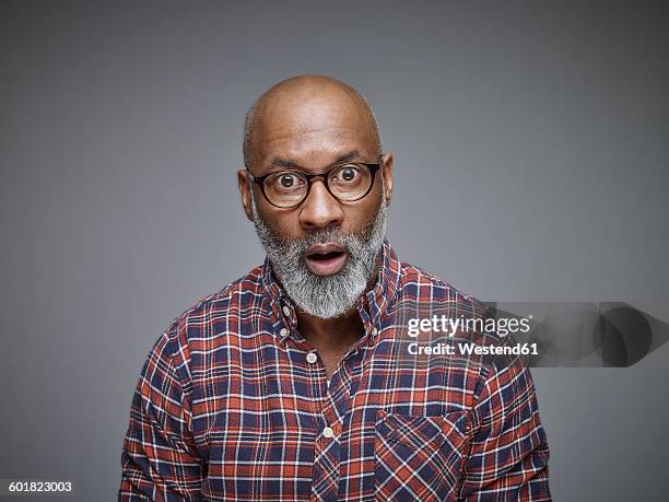 portrait of astonished man wearing spectacles and checked shirt in front of grey background - raised eyebrows stockfoto's en -beelden