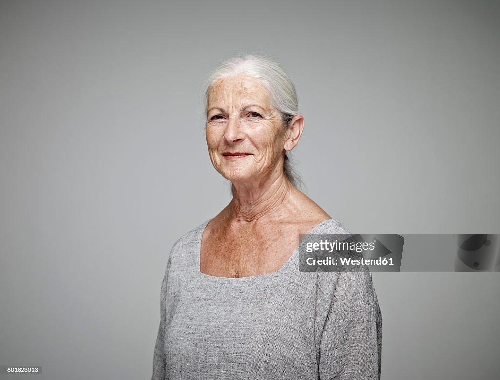Portrait of smiling senior woman in front of grey background