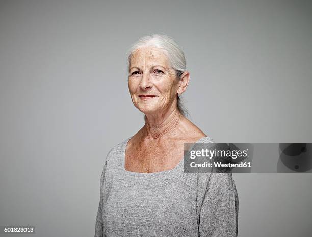 portrait of smiling senior woman in front of grey background - people plain background stock pictures, royalty-free photos & images