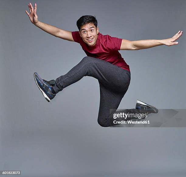 portrait of young man jumping in the air in front of grey background - jumping casual clothing studio shot stock pictures, royalty-free photos & images