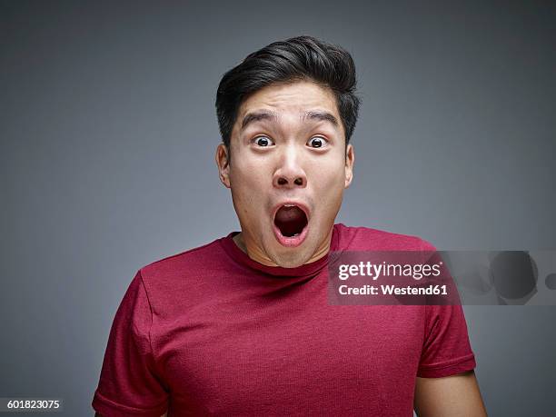 portrait of shocked young man in front of grey background - facing fear foto e immagini stock