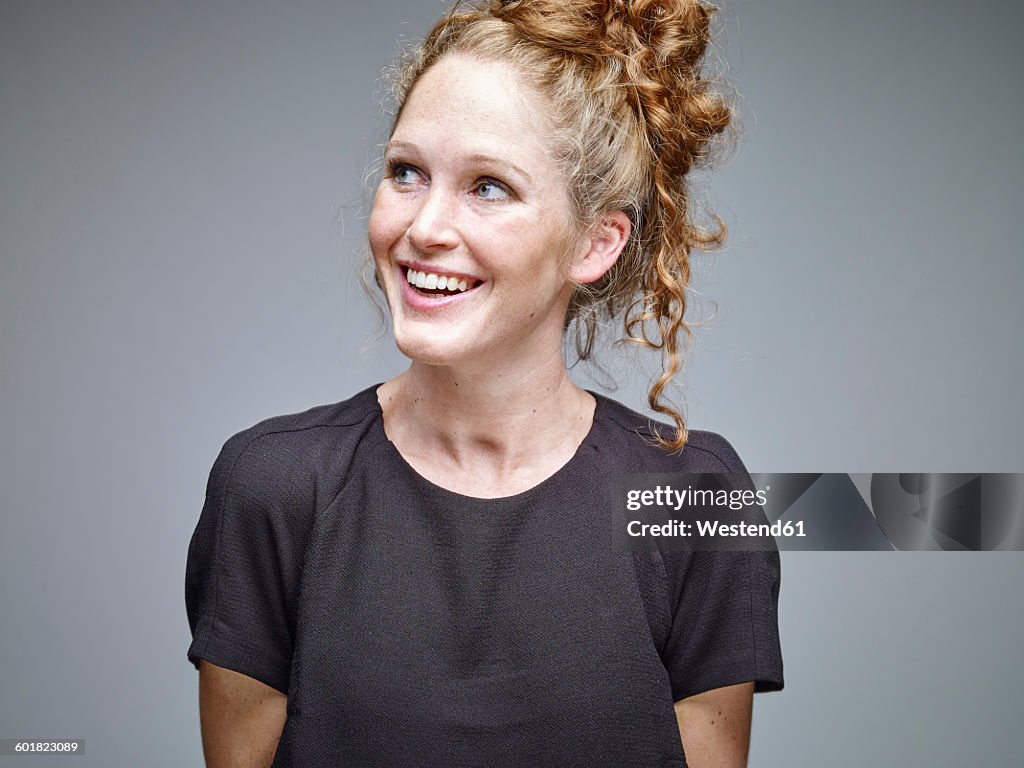 Portrait of smiling young woman with curly blond hair in front of grey background