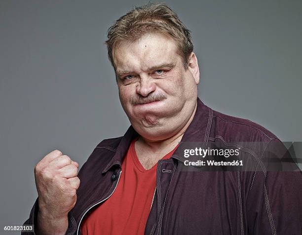 portrait of man clenching his fist in front of grey background - puño gesticular fotografías e imágenes de stock