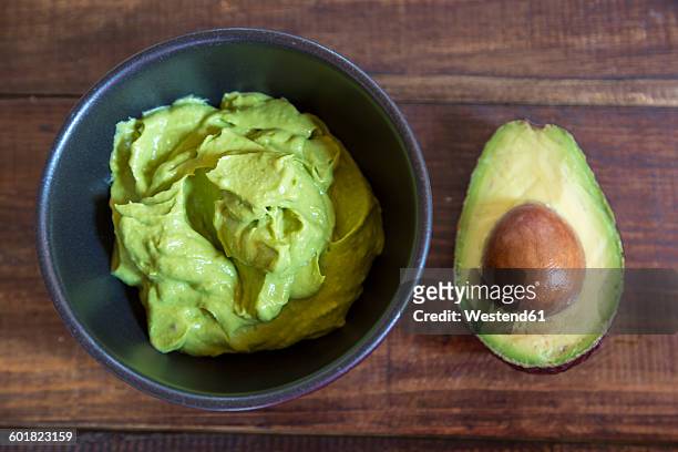 bowl of guacamole and half of an avocado on wood - guacamole stock pictures, royalty-free photos & images