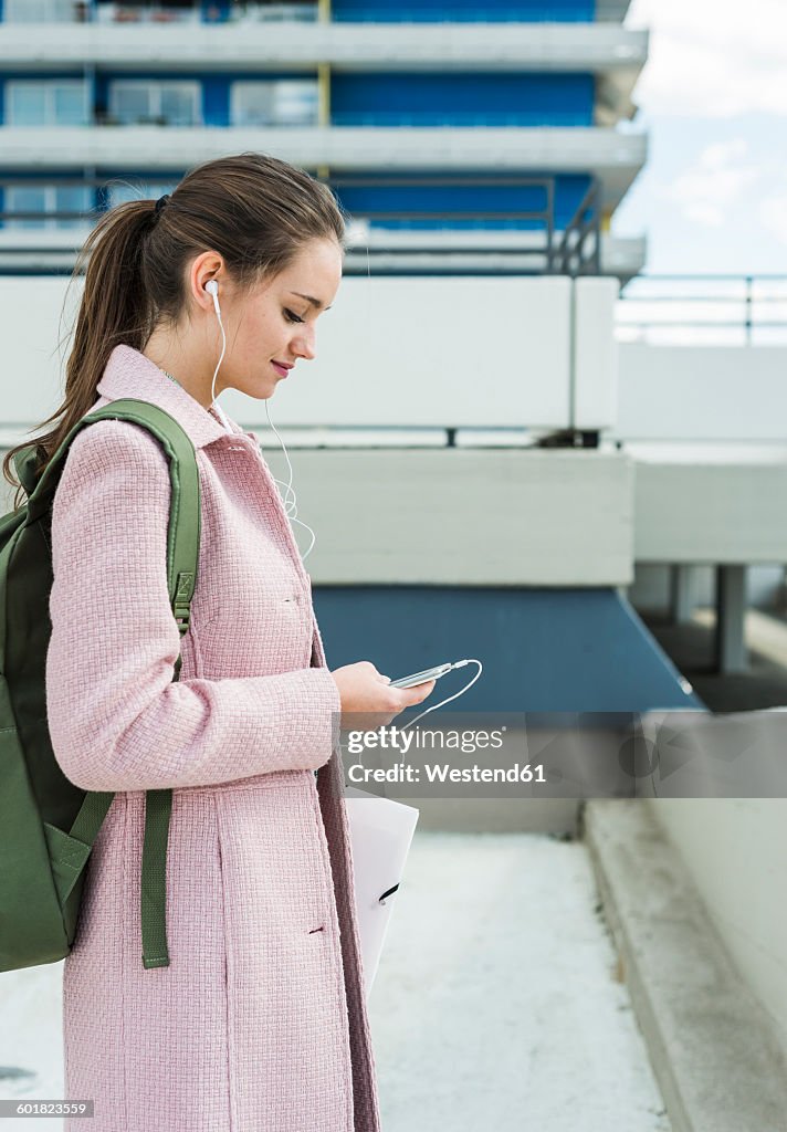 Young woman with earbuds looking at cell phone