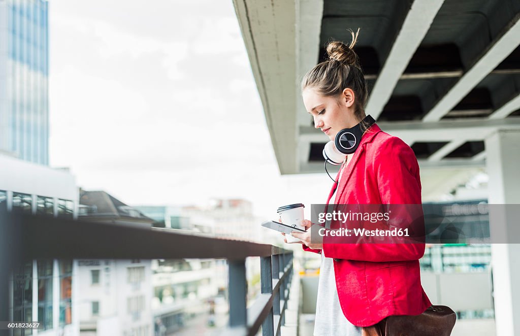 Young woman with coffee to go, headphones and phablet in parking garage
