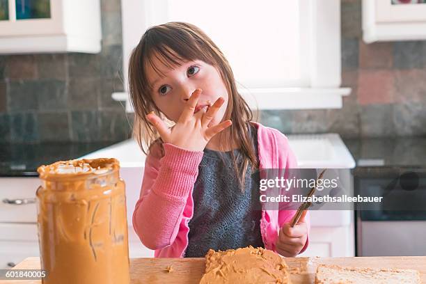 girl making peanut butter sandwich, licking fingers - pindakaas stockfoto's en -beelden