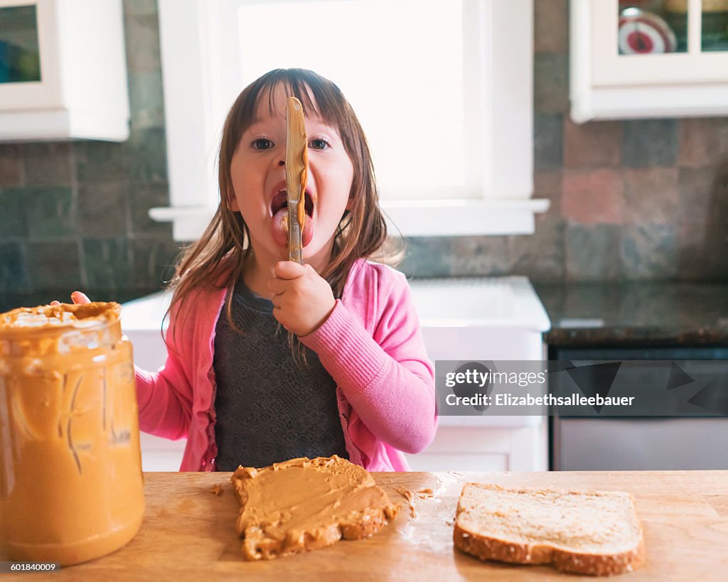 Girl making a peanut butter sandwich, licking the knife