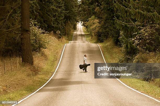 man with guitar case crossed country road - guitar case stock pictures, royalty-free photos & images
