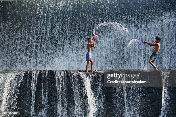 two boys throwing water at each other, tukad unda dam, bali, indonesia - kids fun indonesia stock pictures, royalty-free photos & images