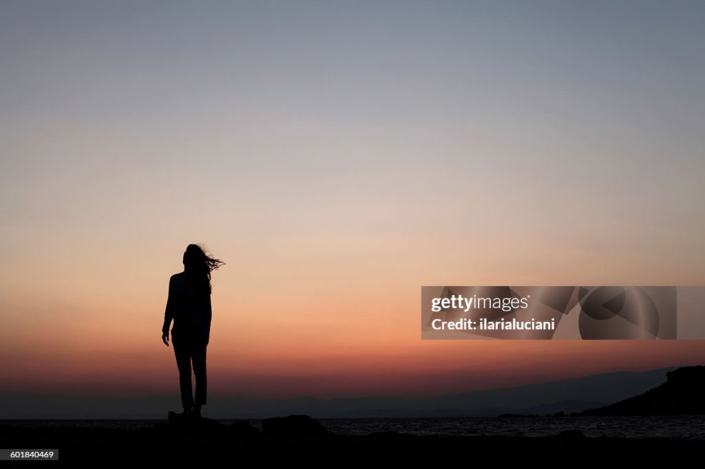 Silhouette of a woman standing outdoors at sunset