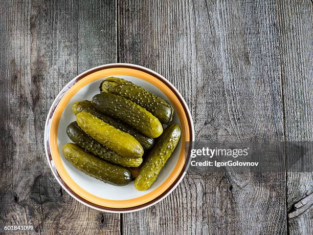 pickled green gherkins in a bowl on a wooden table - essiggurke stock-fotos und bilder