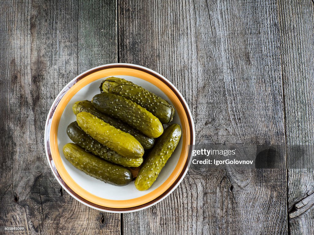 Pickled green gherkins in a bowl on a wooden table