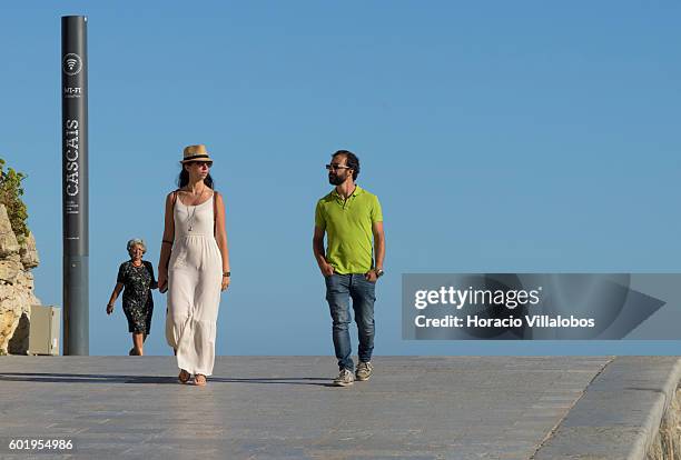 Couple strolls by a free wifi point in Praia da Duquesa on September 09, 2016 in Cascais, Portugal. Although active all year round, Portuguese...