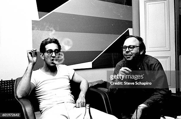 American artist Frank Stella blows smoke rings from a cigar as he sits with curator and historian Henry Geldzahler , New York, New York, 1965.