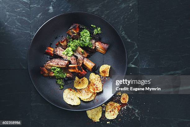 grilled beef ribs with potato chips and parsley sauce - fleisch auf teller stock-fotos und bilder