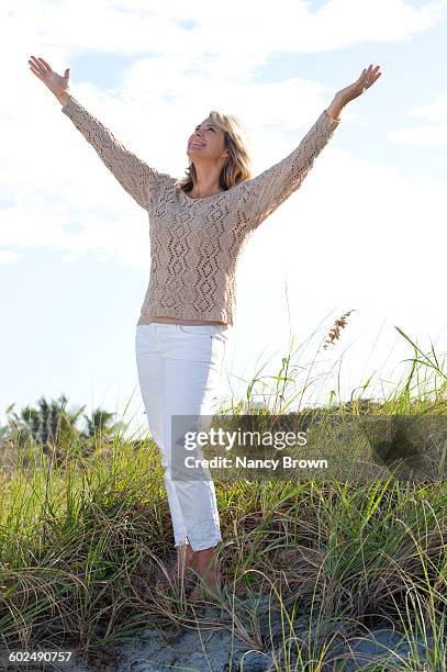 very happy mature (55+) woman standing in dunes - pantalon beige photos et images de collection