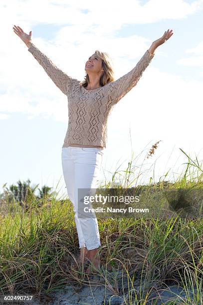 very happy mature (55+) woman standing in dunes - white pants stock pictures, royalty-free photos & images