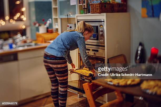 girl taking baking tray with cookies form oven - girls in leggings stock-fotos und bilder