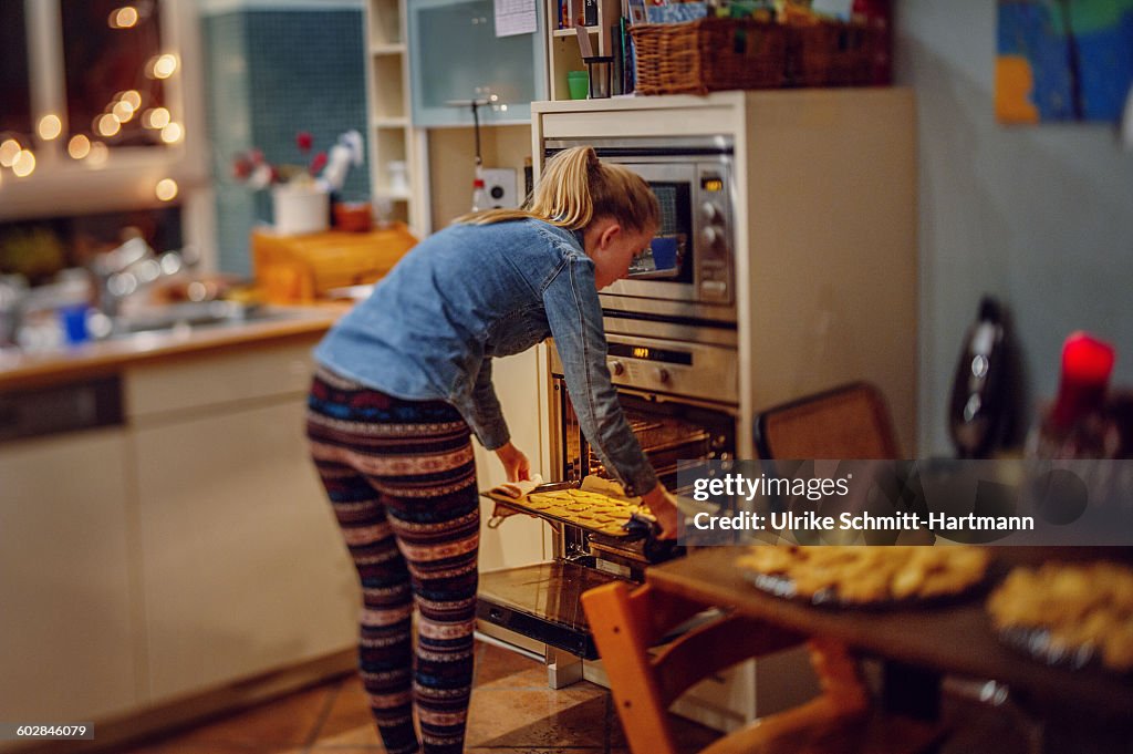 Girl taking baking tray with cookies form oven