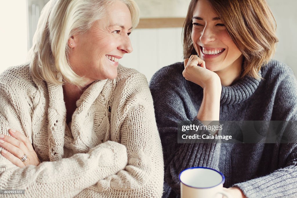 Laughing mother and daughter in sweaters drinking coffee