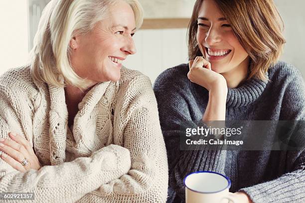 Laughing mother and daughter in sweaters drinking coffee