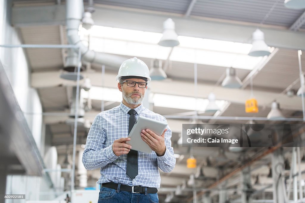 Engineer with hard-hat and digital tablet walking in factory