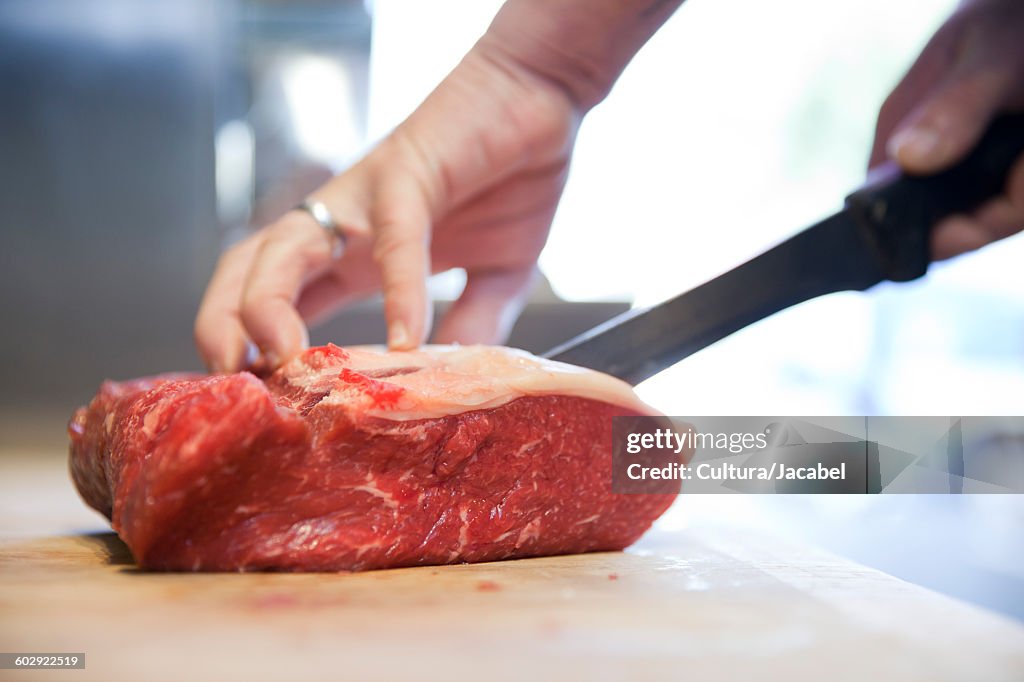 Close up of butchers hands slicing raw steak on butchers block