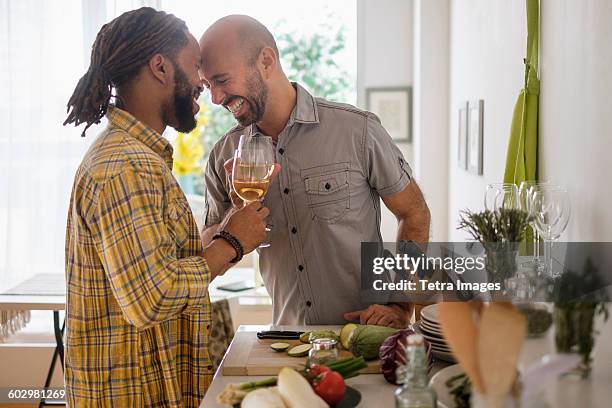 smiley homosexual couple drinking wine in kitchen - dinner date stock pictures, royalty-free photos & images