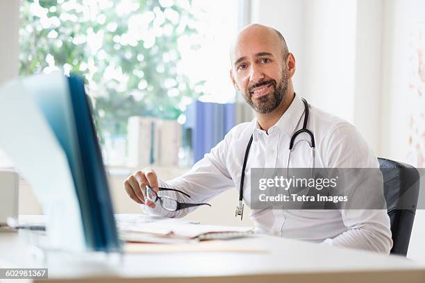 portrait of smiley doctor working with laptop at desk in office - doctor male laptop stock pictures, royalty-free photos & images