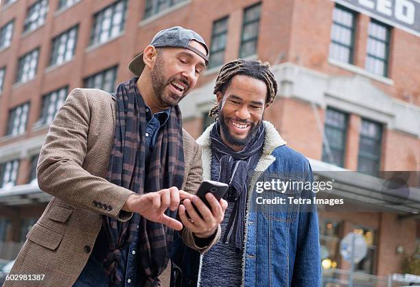 smiley homosexual couple looking at smart phone in street - man showing phone photos et images de collection