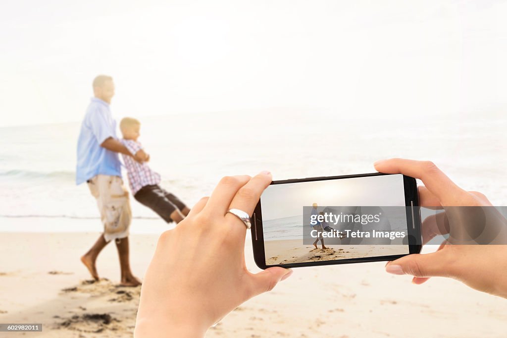 USA, Florida, Jupiter, Young woman photographing father with son (12-13) on beach
