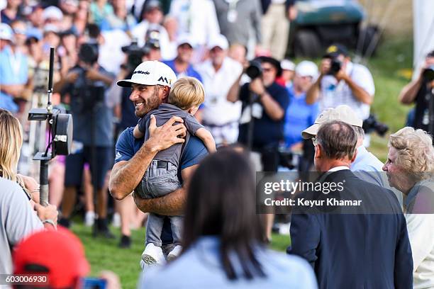 Dustin Johnson smiles and holds his son Tatum following his three stroke victory on the 18th hole green following the final round of the BMW...