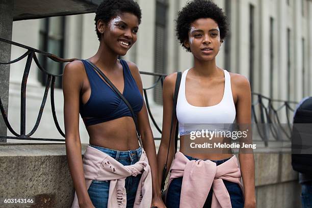 Amilna Estevao, Alecia Morais wear Tommy Hilfiger and Calvin Klein sports bras with pink sweatshirts around their waists, jeans, and black sneakers...