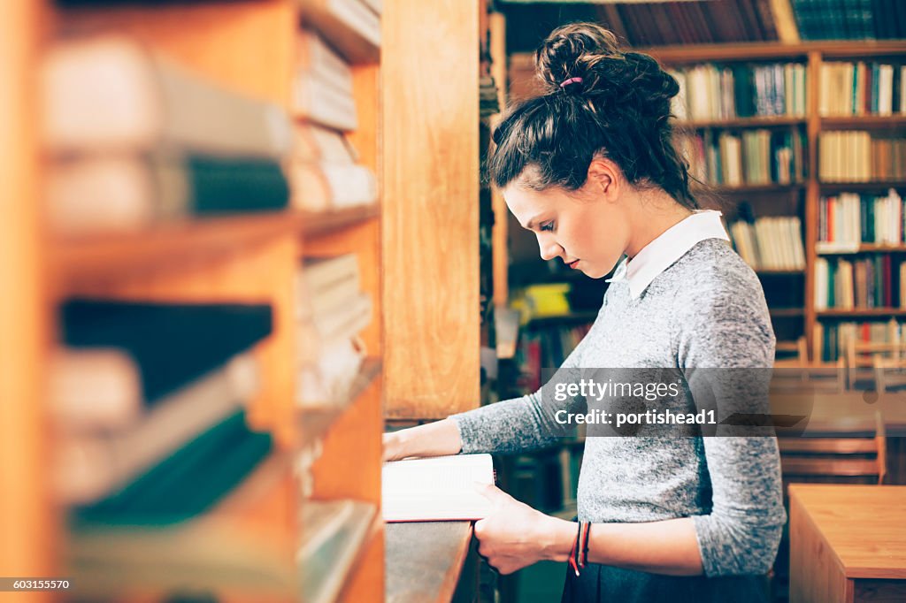 Profile view of young woman reading a book at library