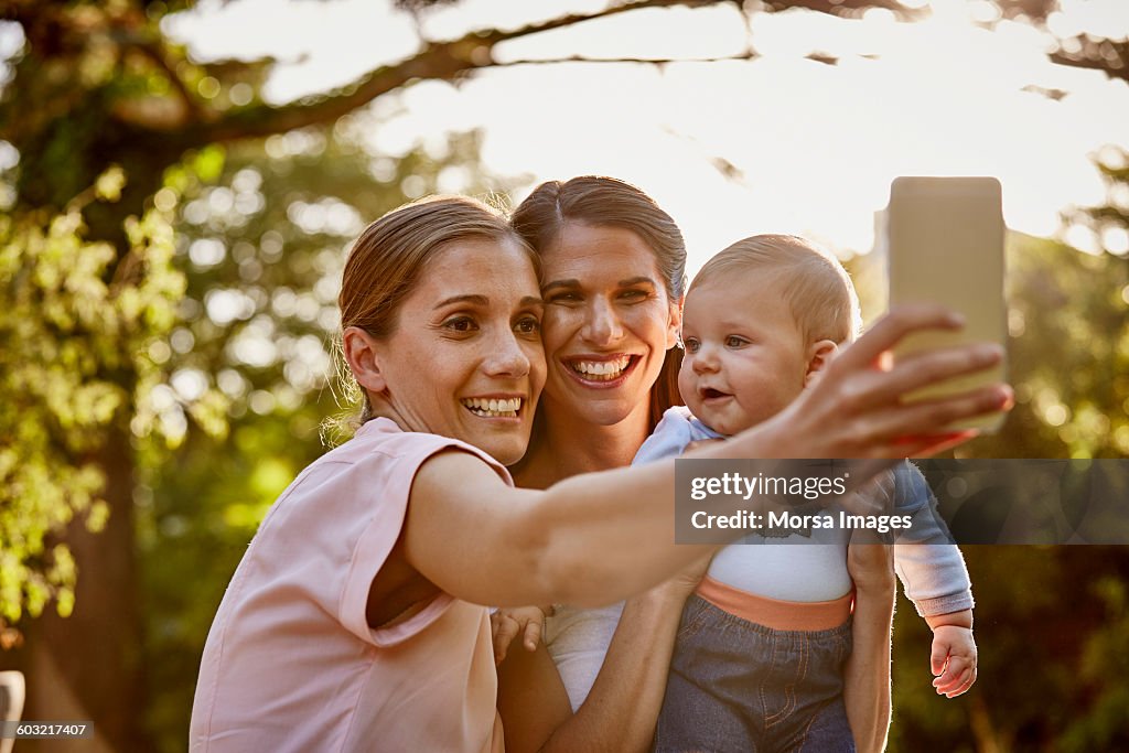 Pareja de lesbianas con bebé tomándose selfie en el parque